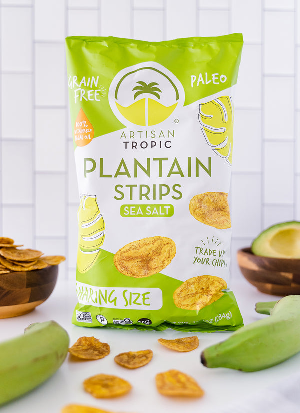 Picture of Artisan Tropic's 10 oz Sea Salt Plantain Strips With Raw Green Plantains and An Avocado in the Background